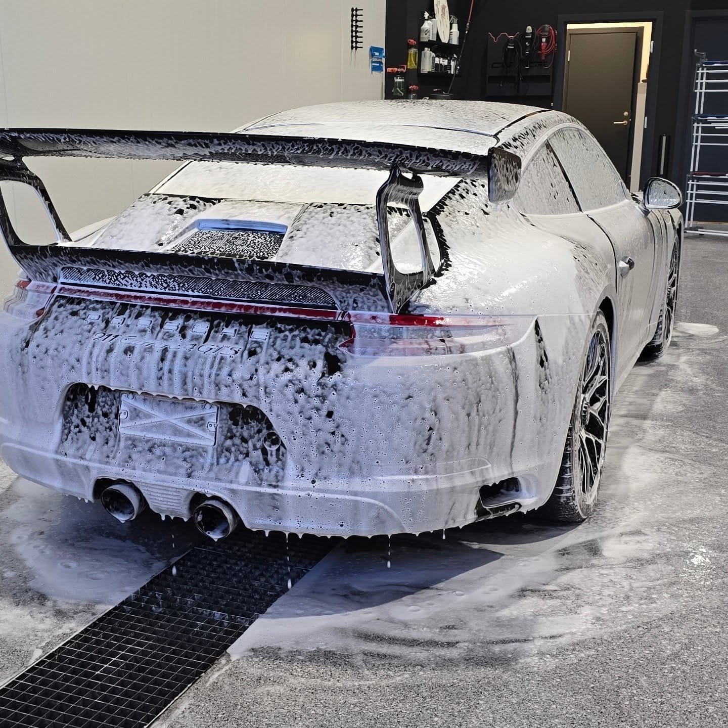 Porsche 911 GT3 dekket av hvitt vaskeskum sett bakfra i vaskehallen